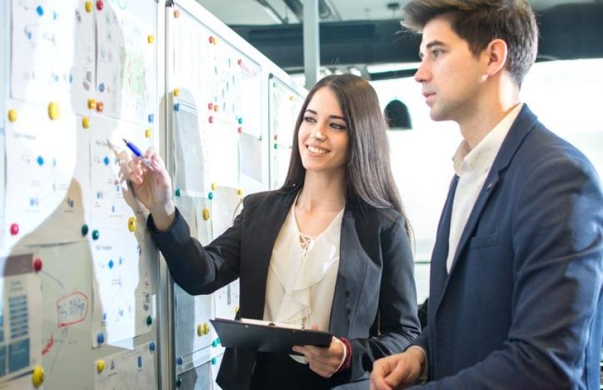Young smiling businesswoman presenting business strategy on board to her male colleague in the board room.