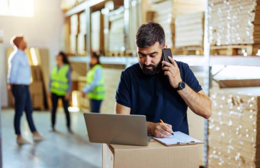 Male warehouse worker looking over the inventory while talking on smartphone.