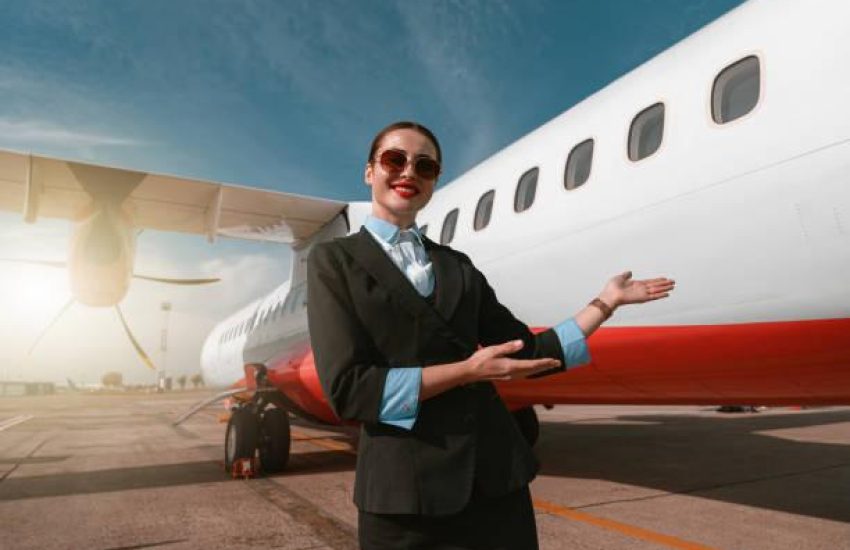 Woman stewardess standing near airplane and inviting on board. Blurred background
