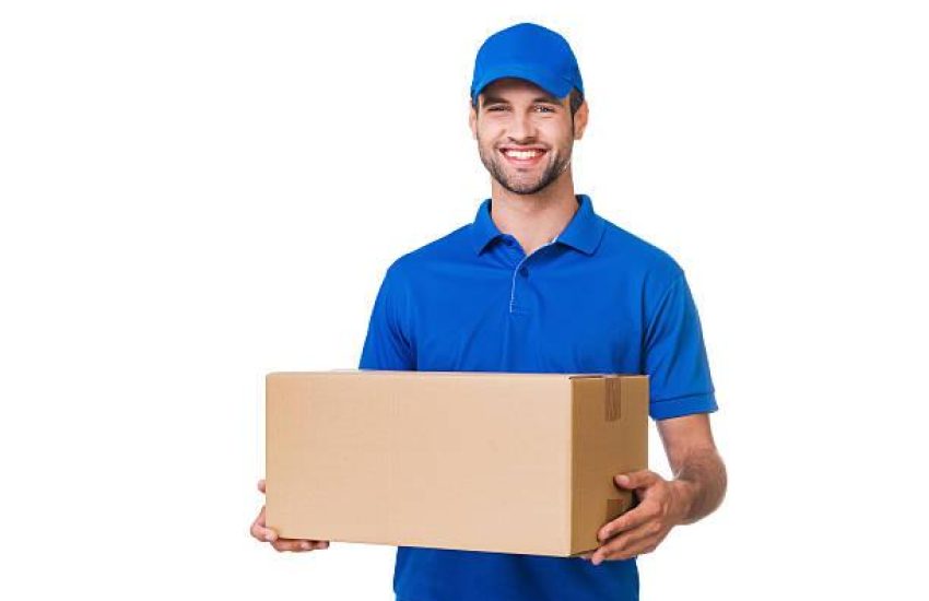 Happy young courier holding a cardboard box and smiling while standing against white background